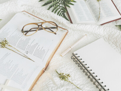 Dos biblias, un anotador, una birome, unos anteojos y las hojas de distintas plantas apoyados sobre una manta blanca