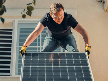 A man stands on a rooftop installing a solar panel