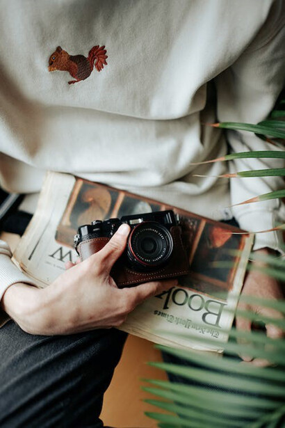 A man seated, clutching a vintage camera in one hand and a newspaper in the other