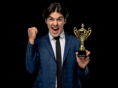 A young, excited, and handsome businessman in a dark blue suit and tie, proudly holding a trophy, representing career success