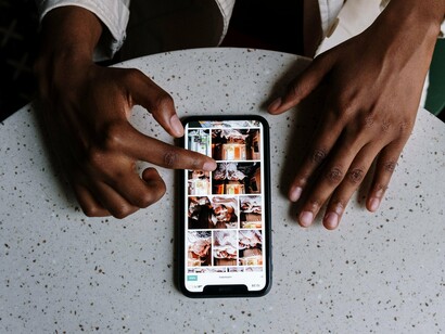 Mãos interagem com um smartphone sobre a mesa de um café, diante de conteúdos exibidos na tela. Cada toque e cada escolha ajudam a alimentar a enorme quantidade de dados utilizada para personalizar nossa experiência digital