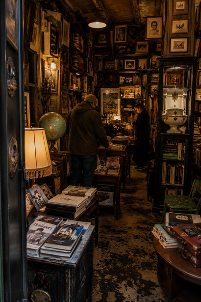 Visitors browsing through a warmly lit vintage bookstore layered with old books, curiosities, and memories