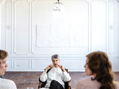 Dressed in a black suit, the female therapist listens attentively from her wooden chair during couples counseling