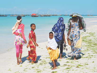 Familia dando un paseo sobre la orilla de una playa en Zanzíbar, Tanzania