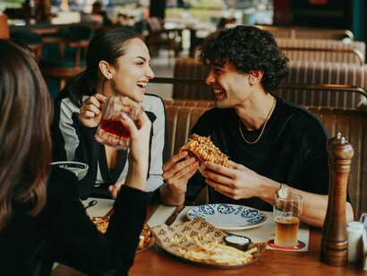 Three friends smiling and chatting over a shared meal, representing the enduring value of face-to-face interaction