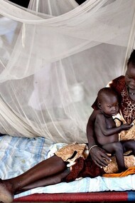 A Nilote woman laying with her baby son and her little daughter standing close by the bed, Africa