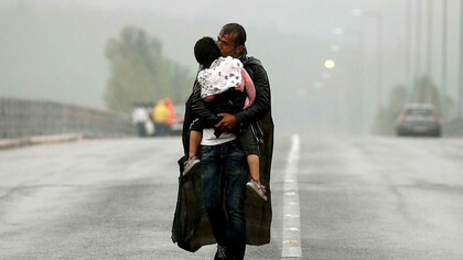 Un refugiado siriio carga con su hija bajo la lluvia al llegar a Grecia