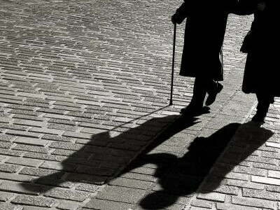 Las sombras de dos ancianos se proyectan contra el adoquinado de una plaza