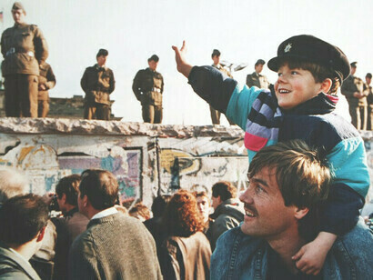 Il ragazzo sulle spalle di suo padre saluta i militari a guardia del muro di Berlino il giorno della sua caduta il 9 novembre 1989, Berlino, Germania