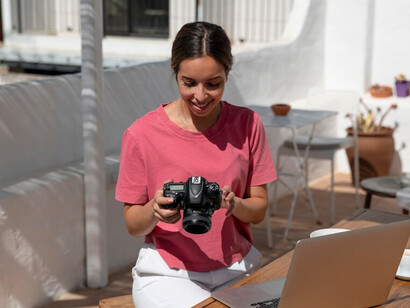 A person working on a laptop at a desk outdoors, with a scenic backdrop and scattered work essentials
