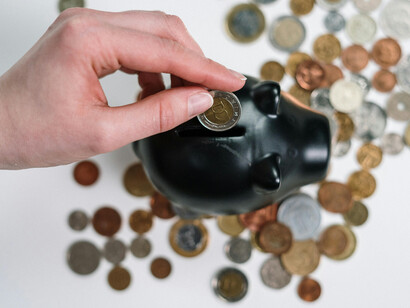 La mano de una persona guardando monedas en una alcancía negra