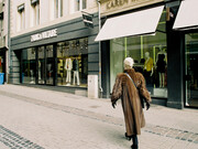 Stylish woman in a brown fur coat passing by the storefronts of high-end brands such as Zadig & Voltaire