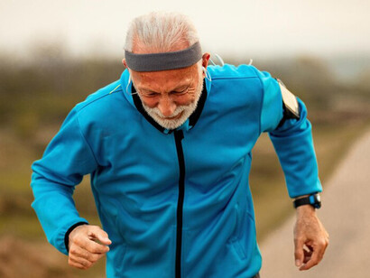 An elderly man jogging through nature, listening to music with earphones, embracing an active and healthy lifestyle