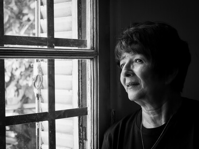 Black-and-white portrait of a grieving elderly woman gazing thoughtfully out of a window, reflecting on loss and cherished memories