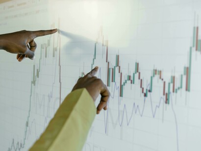 A finger points to a rising graph on a screen, illustrating stock market trends