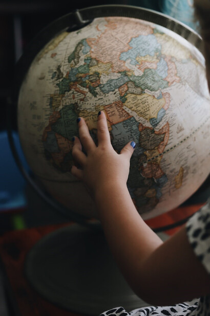 A child reaches out, gently touching a globe ball, as their fingertips explore the contours of our interconnected world 