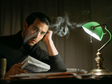 An elegant man sitting at a table reading a book under a retro lamp