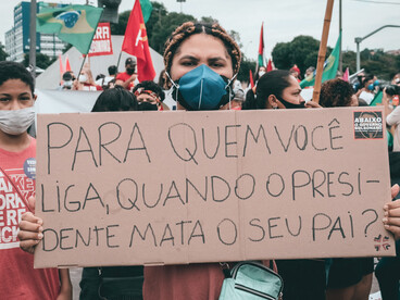 Una joven manifestante con mascarilla sostiene un cartel de cartón con la pregunta de protesta "¿A quién llamas cuando el presidente mata a tu padre?" durante una marcha en la calle