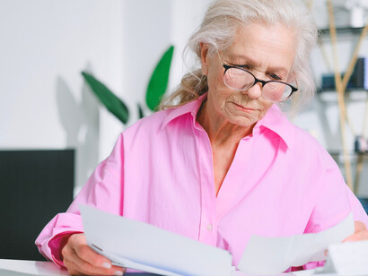 An elderly woman carefully reviewing paperwork, representing the financial uncertainty faced by many pensioners