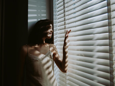Sunlight streaming through hospital window shutters onto a woman looking outside