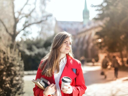 A student holding her notebooks and morning coffee as she prepares for another day in her pursuit of her bachelor of arts degree