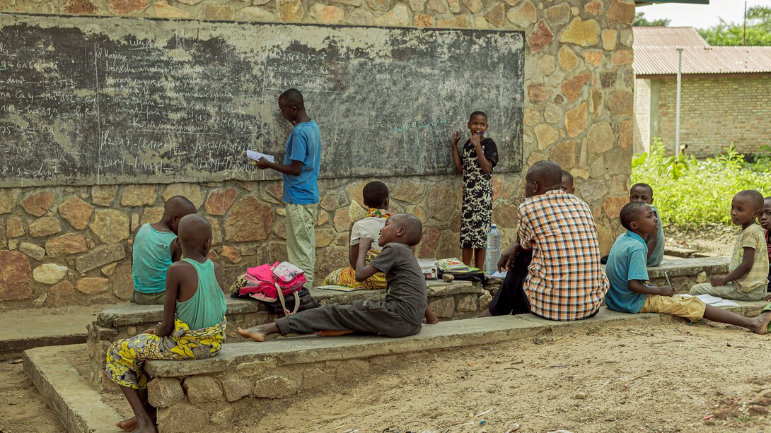 Young students learning beside a weathered chalkboard, symbolising both the resilience of learners and the urgent need for better educational infrastructure