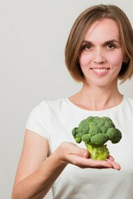 A woman holding a fresh broccoli, emphasizing healthy plant-based nutrition