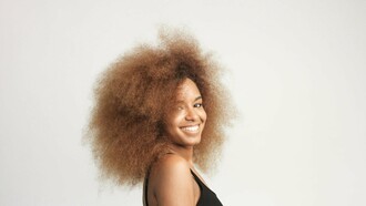 A woman with voluminous hair smiling, showcasing the beauty of natural texture and self-love—celebrating the uniqueness of coily and texturized hair