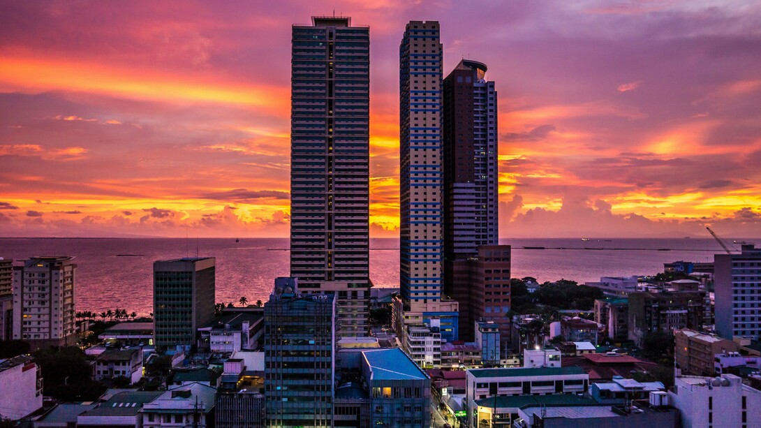 Towering buildings overlooking Manila Bay at dusk, symbolising a city that remains open to history, hope, and endless becoming