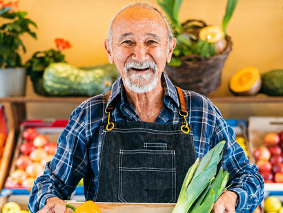 Greengrocer arranging a box of fresh fruits and vegetables outside a local grocery store, showcasing fresh produce and neighborhood commerce