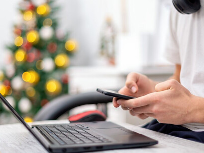 With a smartphone in hand and headphones on, a teenage boy balances a laptop on his knees at home, showcasing the dual-edged nature of technology in children's lives and the potential for digital distractions