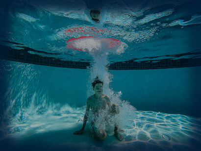 A boy plunges into the swimming pool and sinks to the bottom