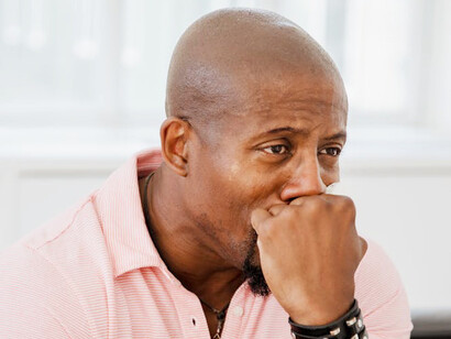 A man sits alone, tears streaming down his face, overwhelmed by the weight of imposter syndrome and the feeling of not deserving his achievements, despite his evident credentials and efforts