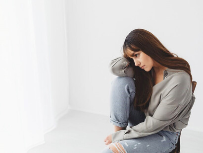 A woman, draped in gray long sleeves, sits on a chair, lost in self-reflective thoughts