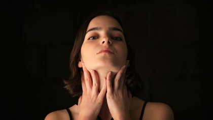 A woman clutching at her sore throat with both hands as it could be due to a case of acid reflux