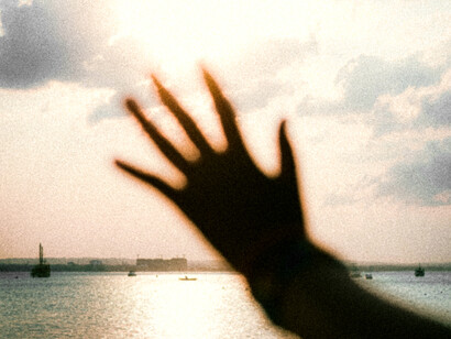 Una mano se alza frente al horizonte marítimo, atravesada por la luz del atardecer