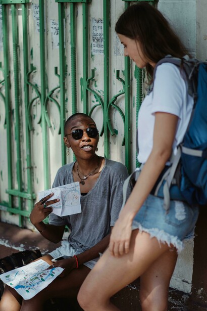 Two female travellers with backpacks studying a map while discovering a lively city street during their journey
