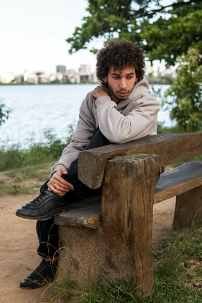 A young man sitting on a park bench with his arms drawn close, symbolising the instinct to withdraw when the possibility of loss feels overwhelming