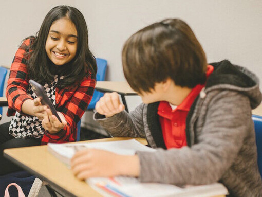 Young students in the classroom enthusiastically sharing something on their phones with each other