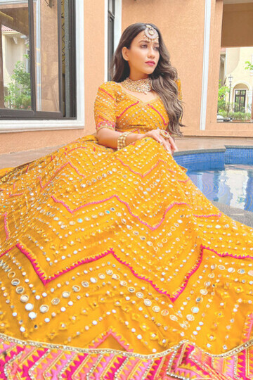 A model showcases a vibrant mustard yellow Phulkari lehenga adorned with exquisite mirror work, zarkan, zari, and detailed thread embroidery