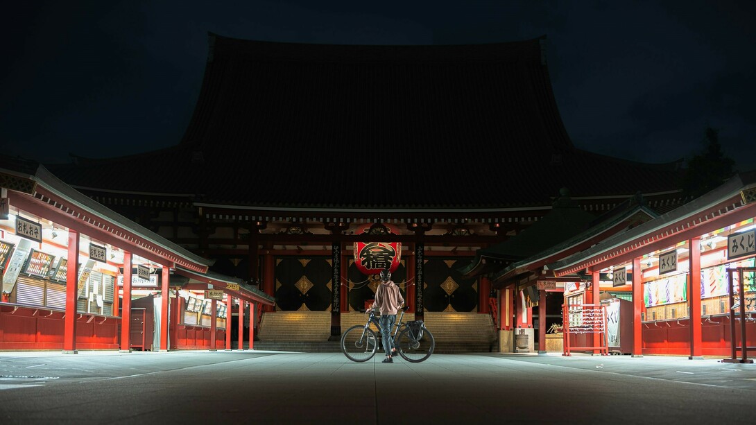 A man riding a bike in front of Sensoji Temple, Asakusa, alone under the moonlight at midnight, with the temple's iconic architecture bathed in soft, serene light, Japan