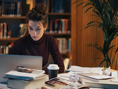 A brunette woman working late at night at her home office, illuminated by the glow of her computer