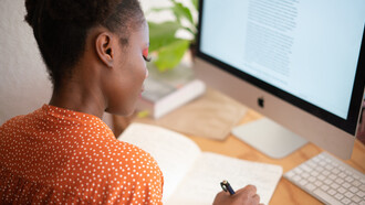 Mulher copia um texto do computador em seu caderno de anotações