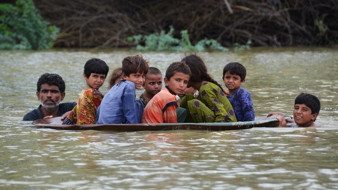 Un par de adultos ayudan a un grupo de niños a cruzar un camino tras las fuertes inundaciones en Pakistán, 2022