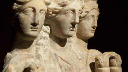 Escultura em mármore da deusa grega Hécate, frequentemente representada em sua forma tríplice. No silêncio da noite, onde o visível se desfaz e o invisível murmura, surge Hécate, a Deusa das encruzilhadas, dos portais e do entre-lugar. Ela não apenas habita o limiar; ela é o limiar. É a senhora das chaves, a portadora da tocha que ilumina não o caminho externo, mas a escuridão interna onde a consciência germina. Hécate ensina que a verdadeira sabedoria nasce quando o indivíduo aceita caminhar entre mundos, atravessando o conhecido e o oculto, confrontando o medo para descobrir o seu próprio poder