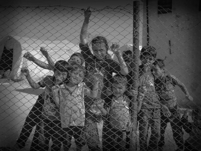 Children look out behind the fence in a refugee camp in Syria during the war