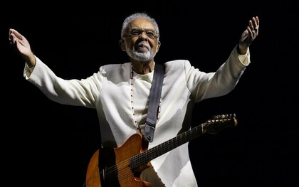 Gilberto Gil no palco, durante a turnê Tempo Rei, no Mineirão, em 2025, com os braços abertos, a guitarra presa ao corpo e um fundo completamente escuro. De braços abertos diante do público, o artista parece acolher as muitas histórias e gerações que sua música acompanhou ao longo de mais de seis décadas de carreira. Do primeiro LP Realce ouvido aos 10 anos ao show de despedida dos grandes palcos, sua música atravessou décadas e se misturou às memórias de uma vida. Sob a luz do palco, a imagem parece traduzir o próprio espírito da canção: o tempo passa, transforma as formas do viver e, ainda assim, algumas músicas permanecem