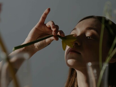 A woman places a flower on her nose and smells it to have a vision
