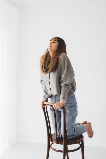 A woman wearing a gray long-sleeved shirt kneeling on a wooden chair