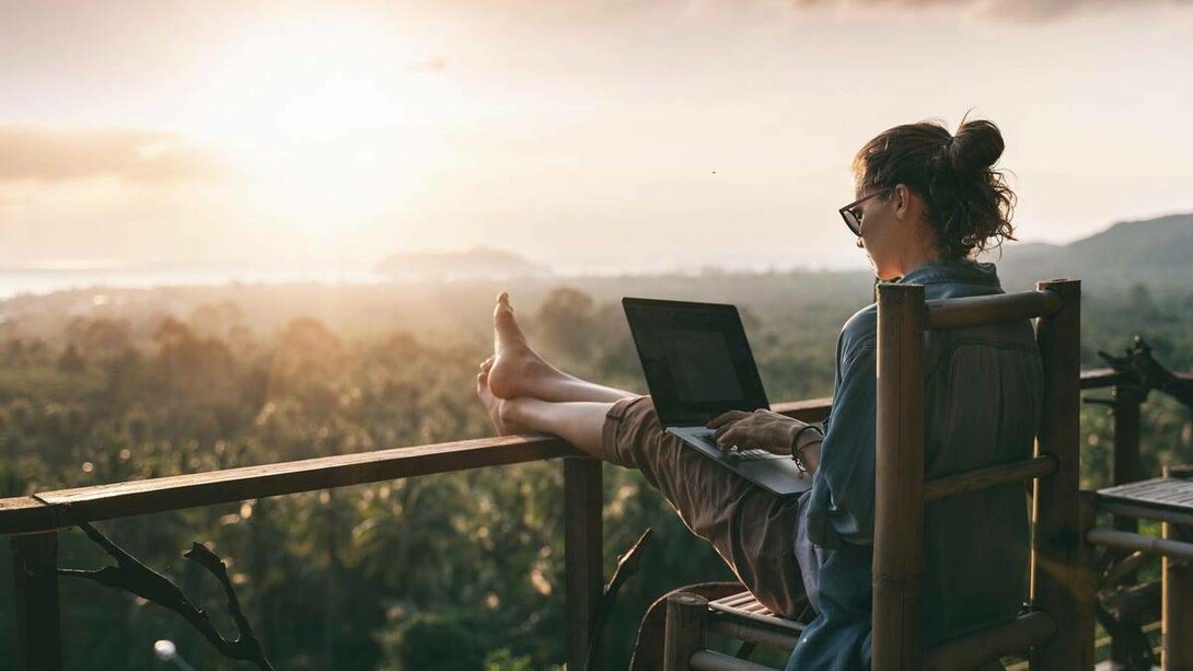 A woman working on her laptop on the balcony overlooking a green field